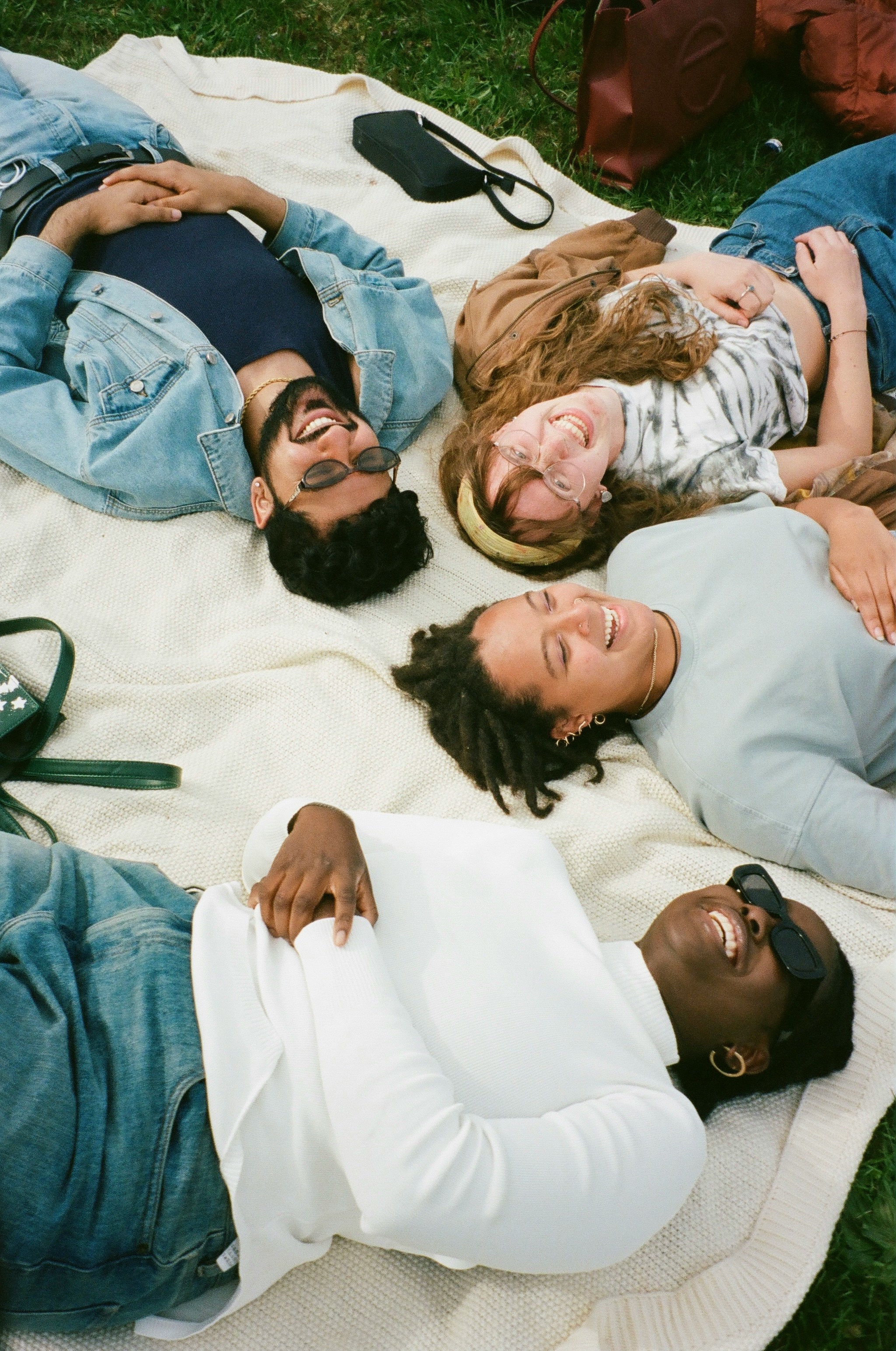 A group of friends lying on a blanket in the grass, laughing together