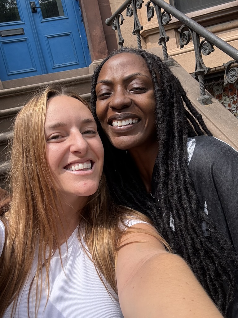 Two friends taking a sunny selfie on a brownstone stoop